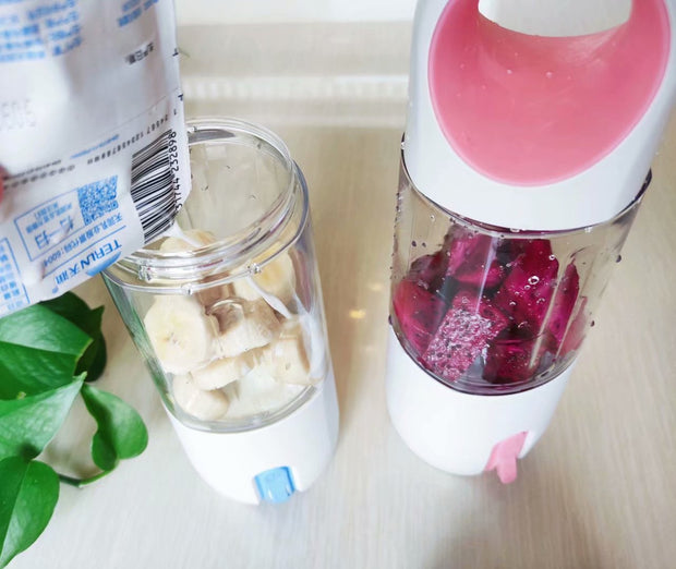 Portable manual electric juicers with pink and blue lids blending bananas and dragon fruit. Compact design for smoothies and fruit drinks.